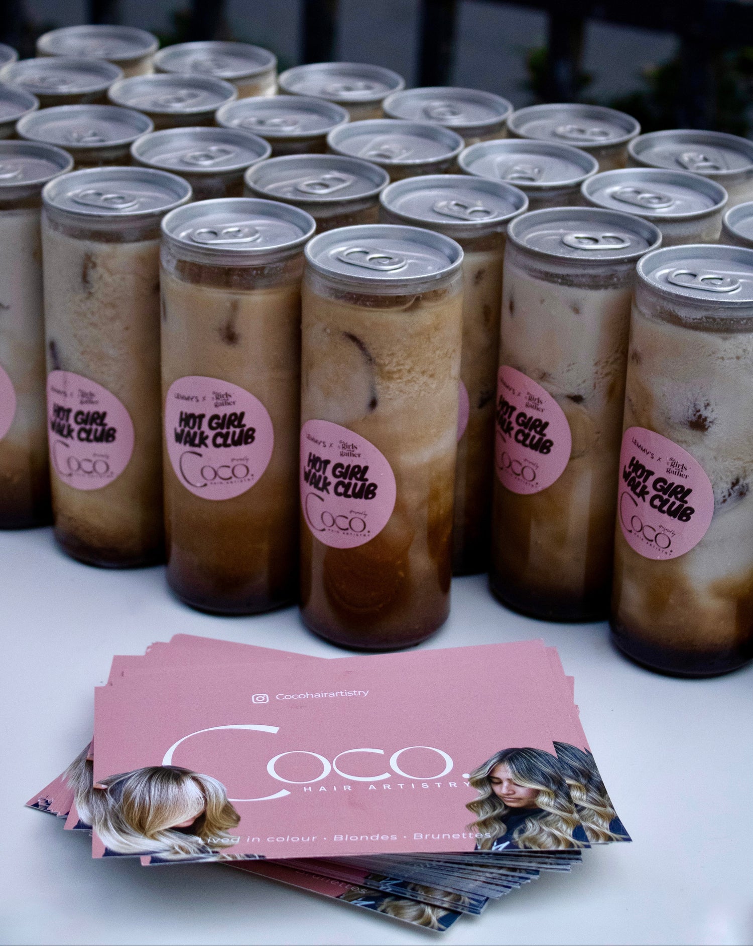 Branded iced coffee drinks prepared for The Girls Who Gather Hot Girl Walk Club, alongside sponsor promotional cards. Complimentary drinks help bring women together after each walk to connect, chat and build new friendships.