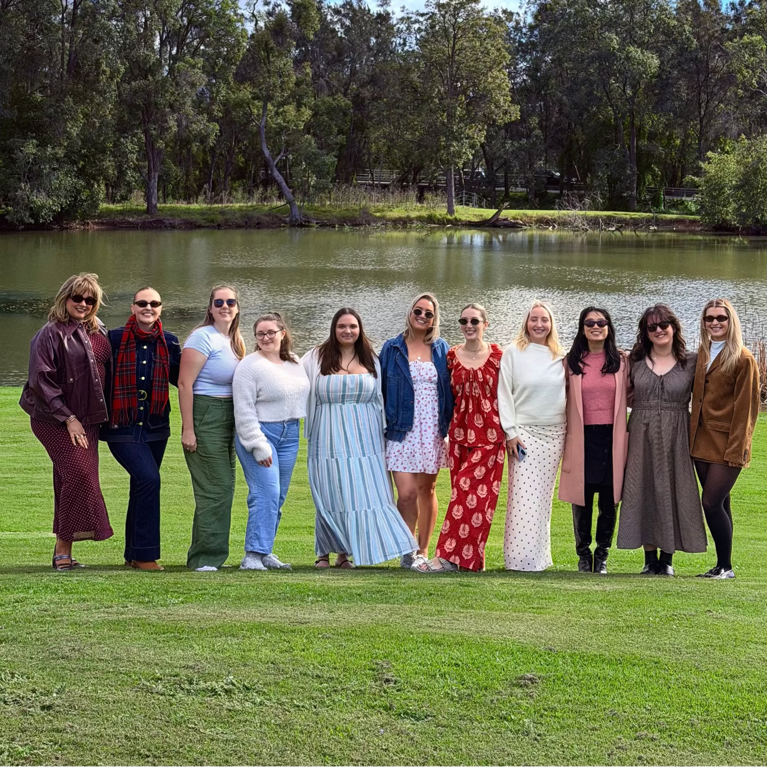 Group of women from The Girls Who Gather posing beside a lake during a Hunter Valley day trip. Women's social event bringing women together to build friendships, explore the Hunter Valley and create meaningful connections.